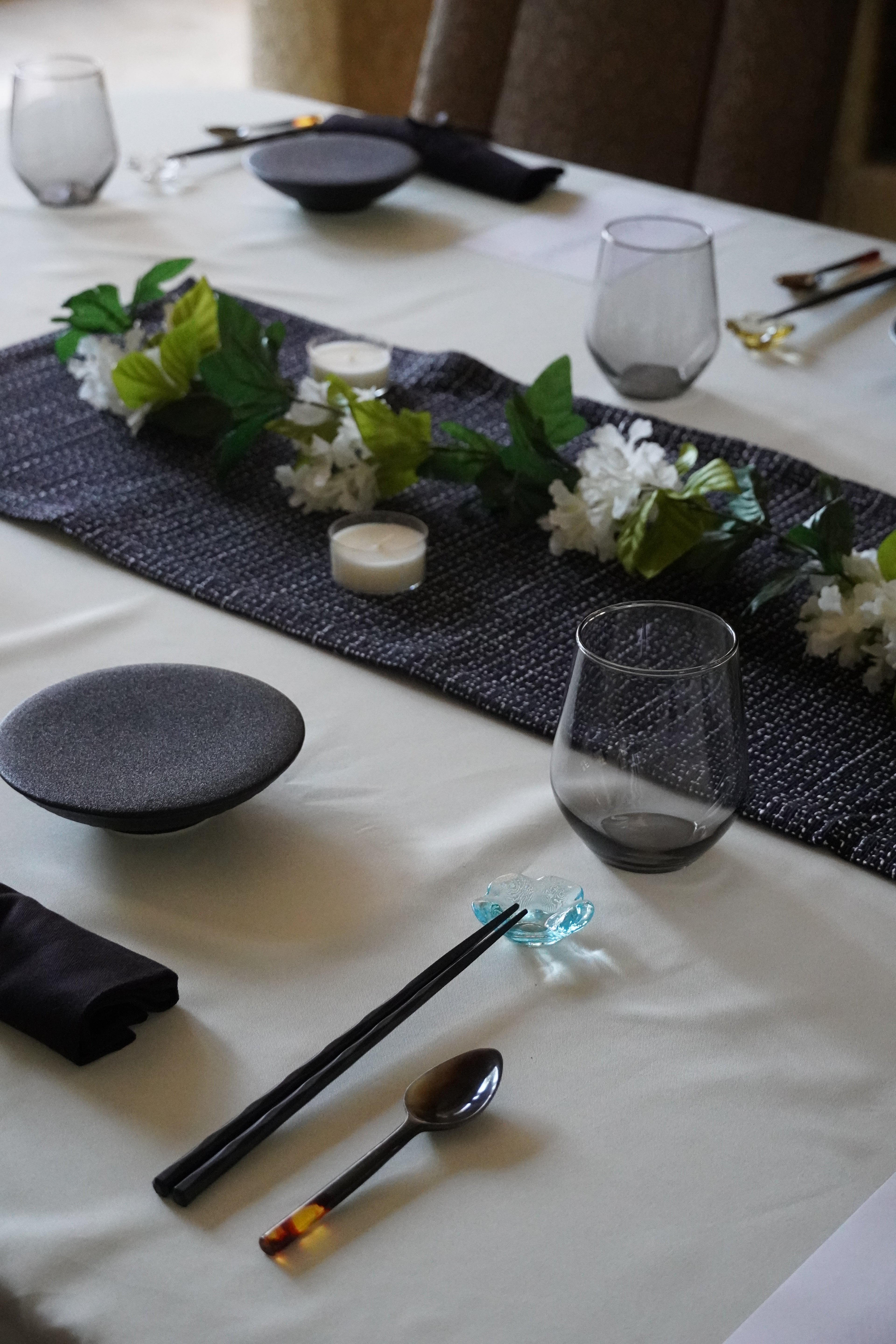 Table setting with cutlery, glasses, and floral decorations on a white tablecloth.