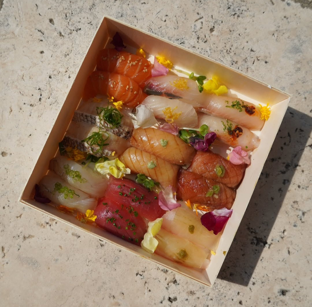Assorted sushi in a cardboard box on a concrete surface